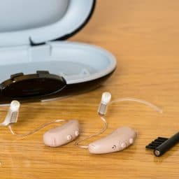 Close up of hearing aids, with a cleaning brush and storage case.