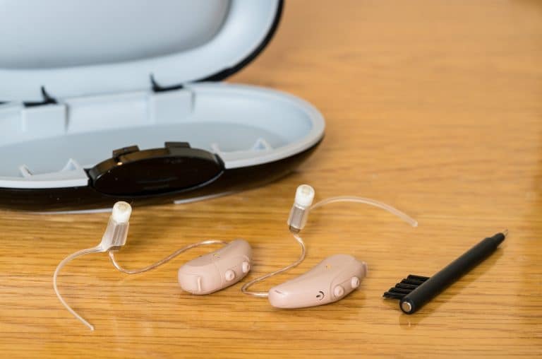 Close up of hearing aids, with a cleaning brush and storage case.