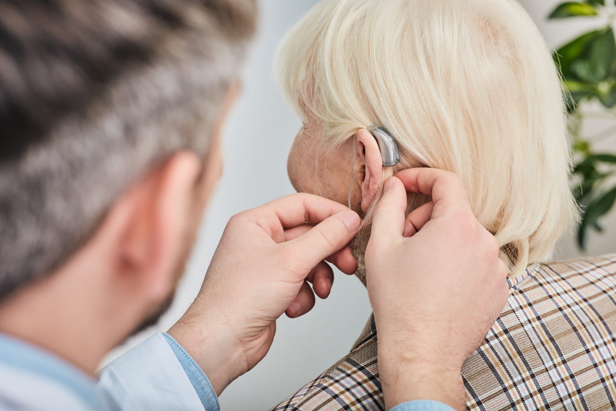 Audiologist helping to fit hearing aid on to woman's ear.