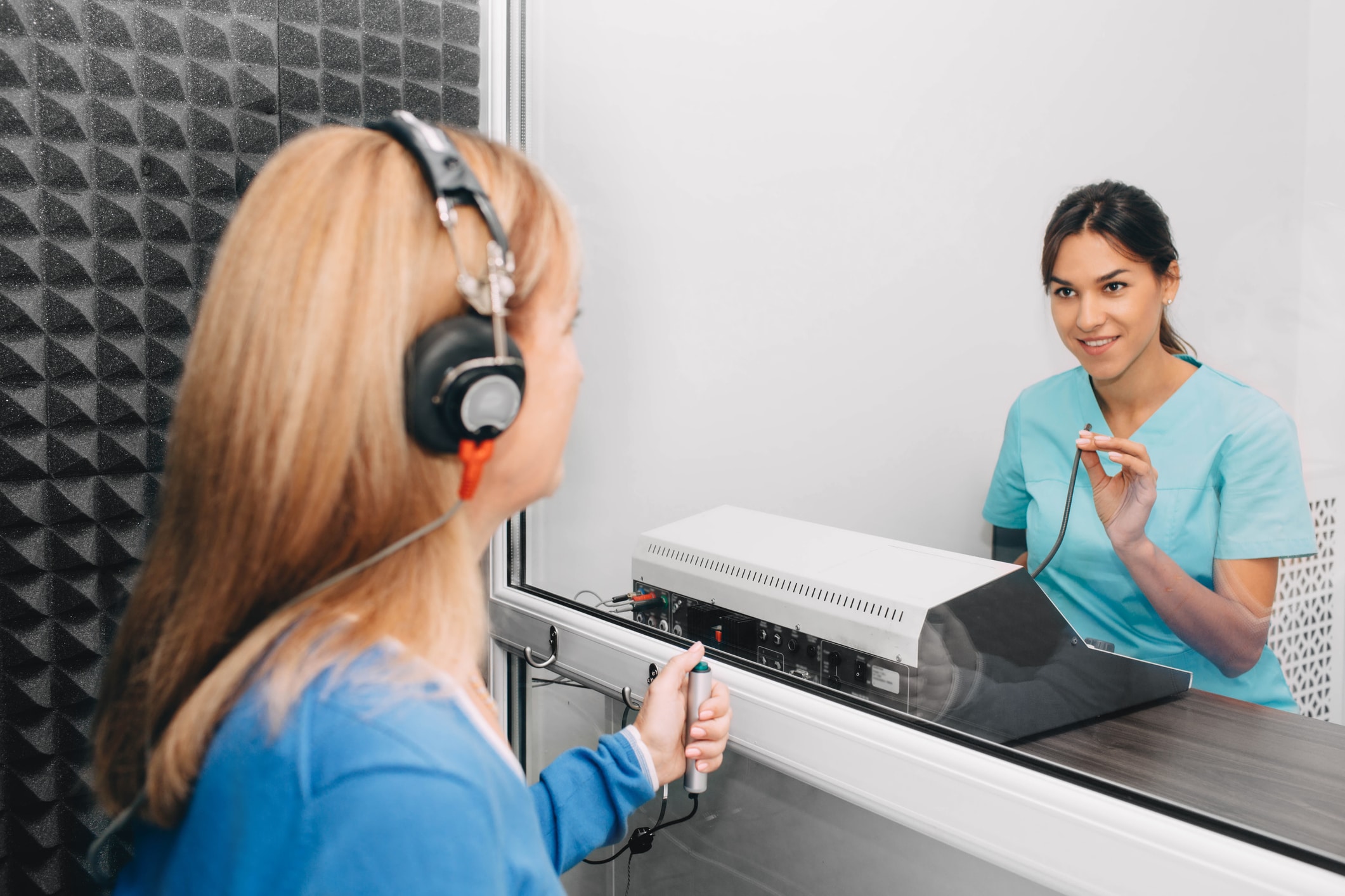 audiologist doing hearing exam to a mature patient using audiometer in special audio room.