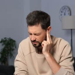 Man with tinnitus holds finger to ear