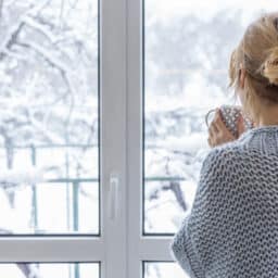 Woman holding a mug of tea looking out a window at the snow