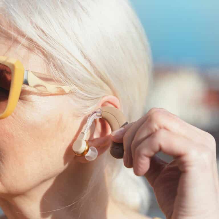 Woman with sunglasses inserting a hearing aid Woman with sunglasses inserting a hearing aid