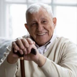 happy senior gentleman with white hair sitting on a couch, holding his cane in his hand