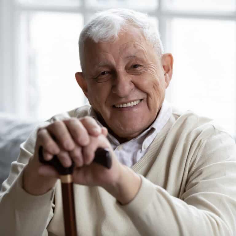Happy senior grandfather sitting on couch smiling happy senior gentleman with white hair sitting on a couch, holding his cane in his hand