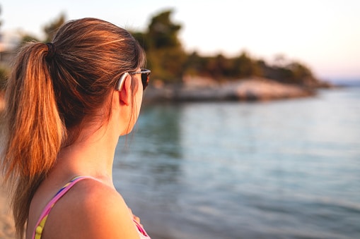 Young woman with hearing aids enjoys a sunny day on the beach.