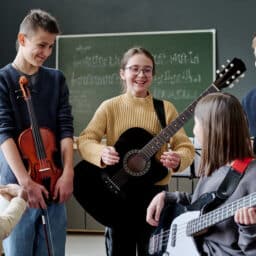 Group of cheerful teen boys and girls with musical instruments having break during rehearsal in classroom