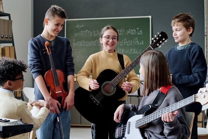 Middle School Students At Music Class Group of cheerful teen boys and girls with musical instruments having break during rehearsal in classroom
